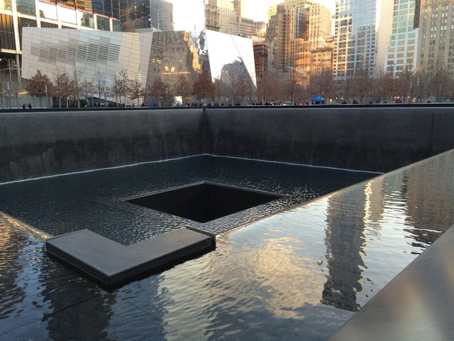 the photo shows the north pool at the 9/11 memorial in new york city, featuring cascading water and surrounding city buildings.