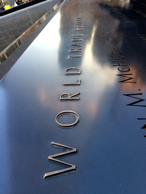 close up of engraved names on the world trade center memorial, with "world trade center" prominently visible on the reflective surface.