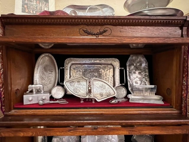 a wooden display cabinet with shelves holding various ornate silver items, including trays, boxes, a hairbrush, scissors, and decorative dishes, arranged on a red velvet lining.