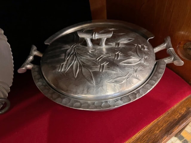 a round metal dish with a lid, decorated with an embossed bamboo leaf pattern, is displayed on a red velvet surface.