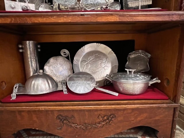 a collection of silver plated serving dishes, plates, and utensils is displayed on a red velvet lined wooden shelf.