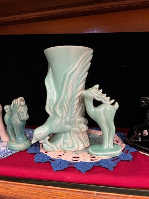 mint green ceramic vase featuring a bird with outstretched wings and a small deer, displayed on a doily with other ceramic figurines.