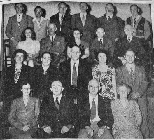 black and white photo of eighteen adults, ten men and eight women, arranged in three rows, posing formally and facing the camera.