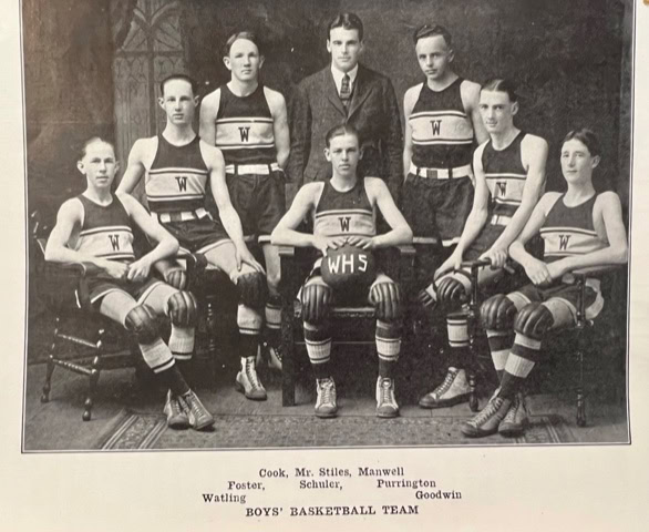 black and white photo of a boys’ basketball team in uniforms labeled "wh" posing with their coach; a basketball marked "whs" is held by one player.