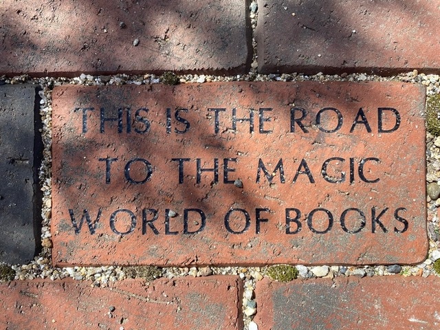 a red brick walkway features an engraved brick with the words: "this is the road to the magic world of books.