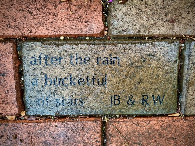 a brick engraved with the words: "after the rain a bucketful of stars jb & rw" set among other bricks on a walkway.