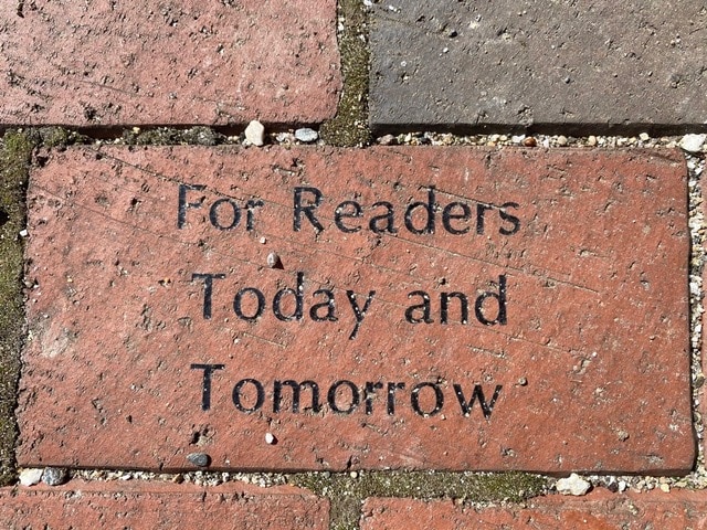 a red brick engraved with the words "for readers today and tomorrow" set among other bricks and gravel.