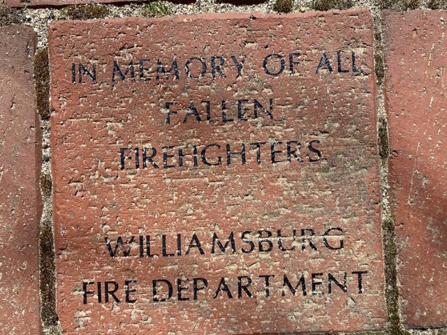 a brick reads "in memory of all fallen firefighters williamsburg fire department," engraved in black text.