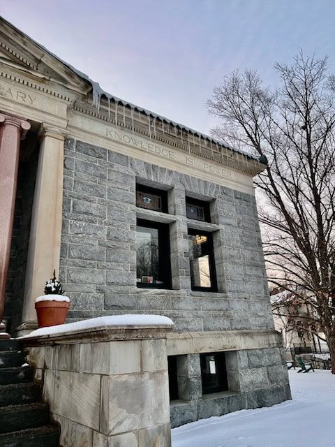 gray stone building with icicles along the roof, snow on the ground, and the phrase "knowledge is power" engraved above the windows.