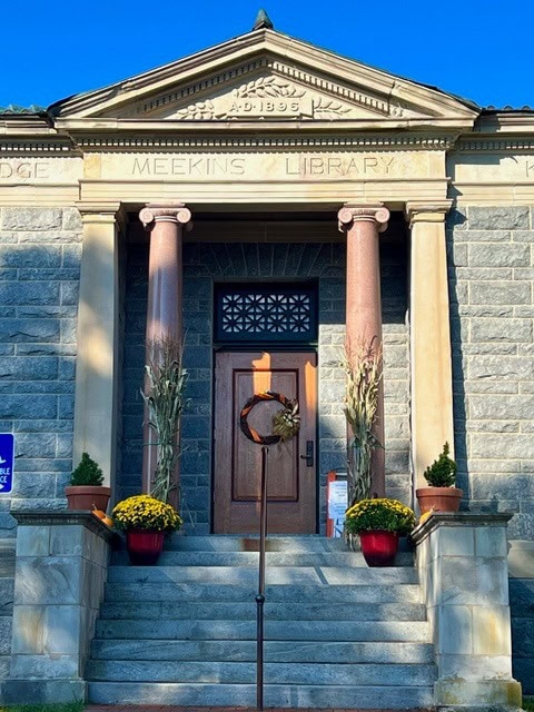 stone building entrance with columns, labeled "meekins library," decorated with yellow flowers and cornstalks on either side of the steps.