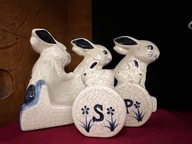 three ceramic rabbit figurines with blue floral designs, two holding round containers labeled "s" and "p," placed on a maroon surface.