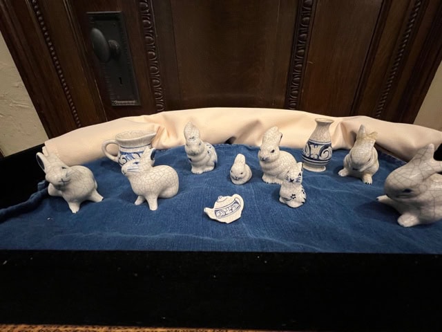 a collection of small blue and white ceramic animal figurines and vases displayed on a blue cloth in front of a wooden background.
