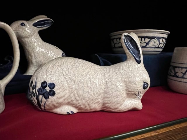 ceramic rabbit figurines with blue floral designs are displayed on a red cloth next to pottery bowls with blue patterns.