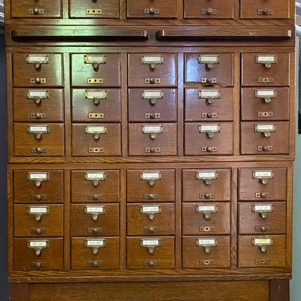 a wooden library card catalog cabinet with multiple small labeled drawers and metal handles.