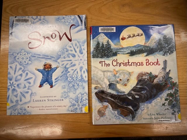 two children's books on a wooden table: "snow" featuring a child in a snowflake scene, and "the christmas boot" with animals and a boot under a snowy night sky.