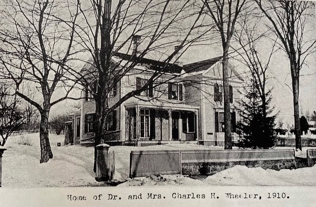 black and white photo of a two story house with trees in front and snow on the ground. caption reads, "home of dr. and mrs. charles h. wheeler, 1910.