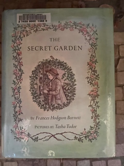 a copy of "the secret garden" by frances hodgson burnett, featuring an illustrated cover of a child opening a door, with pictures by tasha tudor.