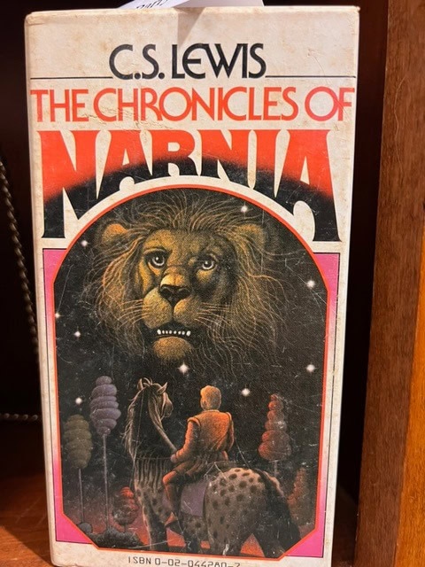 book cover of "the chronicles of narnia" by c.s. lewis, featuring a lion's face and a person riding a horse or similar animal in a forest at night.