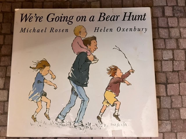 cover of the book "we're going on a bear hunt" by michael rosen and helen oxenbury, showing an adult carrying a child with three children walking.