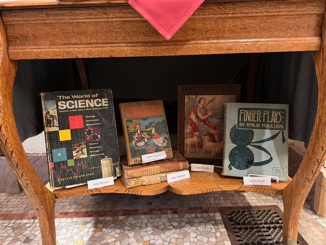a wooden table displays five vintage books with title cards, including "the world of science," "hans brinker," "old testament stories," and "finger plays by emilie poulsson.