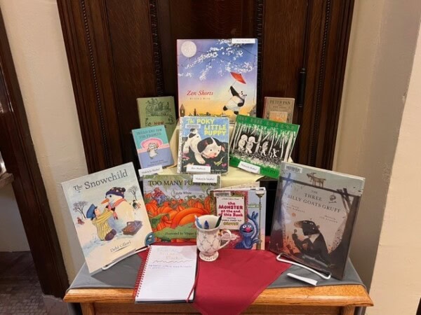 a display of children's books arranged on a wooden surface, with a red napkin, a tea cup, a notepad, and a pen in front.
