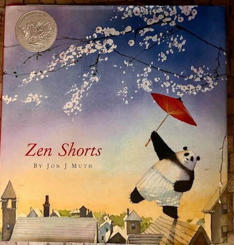 the cover of the book "zen shorts" by jon j muth featuring a panda holding a red umbrella, floating above rooftops with cherry blossom branches and a medal in the top left corner.