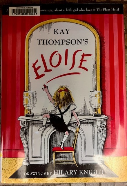 book cover of "eloise" by kay thompson, featuring an illustration of a girl with messy hair sitting on a chair, writing her name on a large mirror above a decorative table.