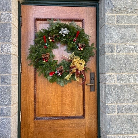 a wooden door with a festive holiday wreath decorated with red berries, pinecones, and a gold ribbon, set in a stone wall.