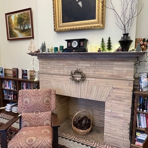 a fireplace decorated with pinecones, small trees, and a clock sits between bookshelves in a cozy room with framed art and an upholstered chair.