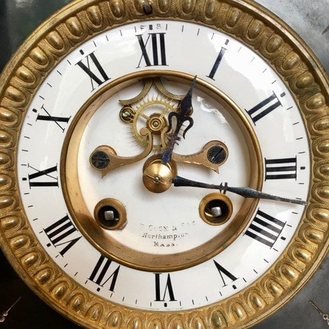 close up of an antique clock face with roman numerals, ornate gold trim, and visible clockwork gears. the time shown is approximately 10:05:19.