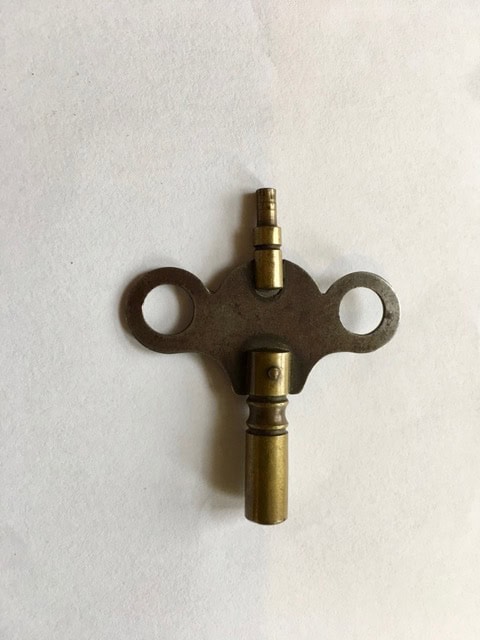a metal clock winding key with two round handles lying on a white surface.