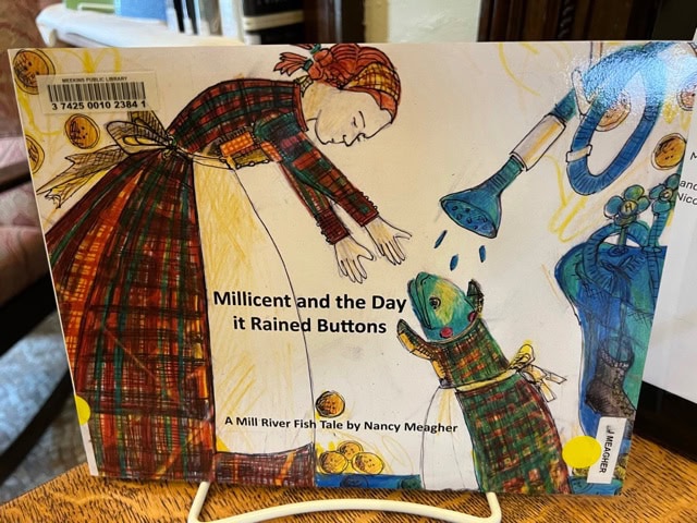 a woman and a dog wearing plaid clothes stand outside as buttons fall from the sky; the book cover reads "millicent and the day it rained buttons" by nancy meagher.