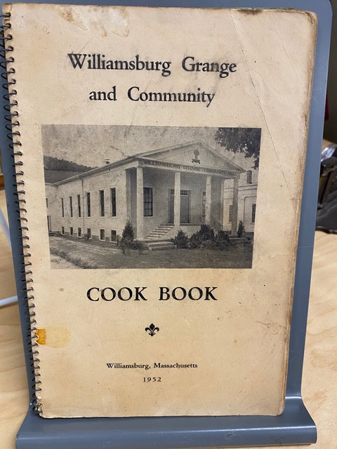a spiral bound 1952 cookbook titled "williamsburg grange and community cook book" with a black and white photo of a building on the cover.