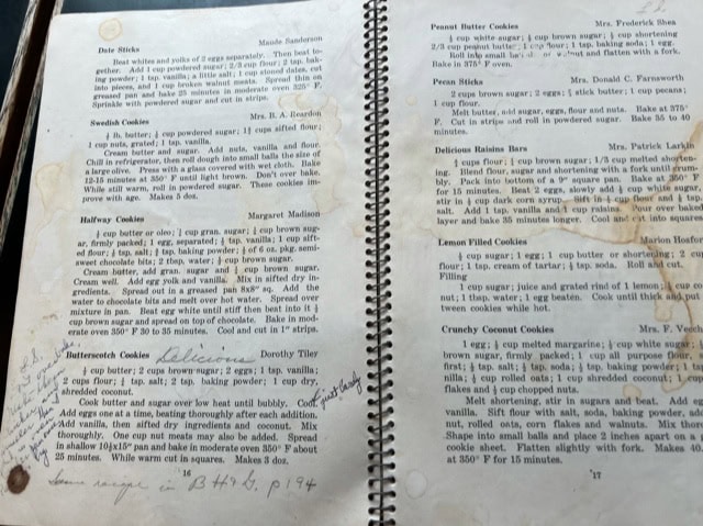 two open pages of a spiral bound cookbook show various cookie recipes, handwritten notes, and visible stains on the paper.