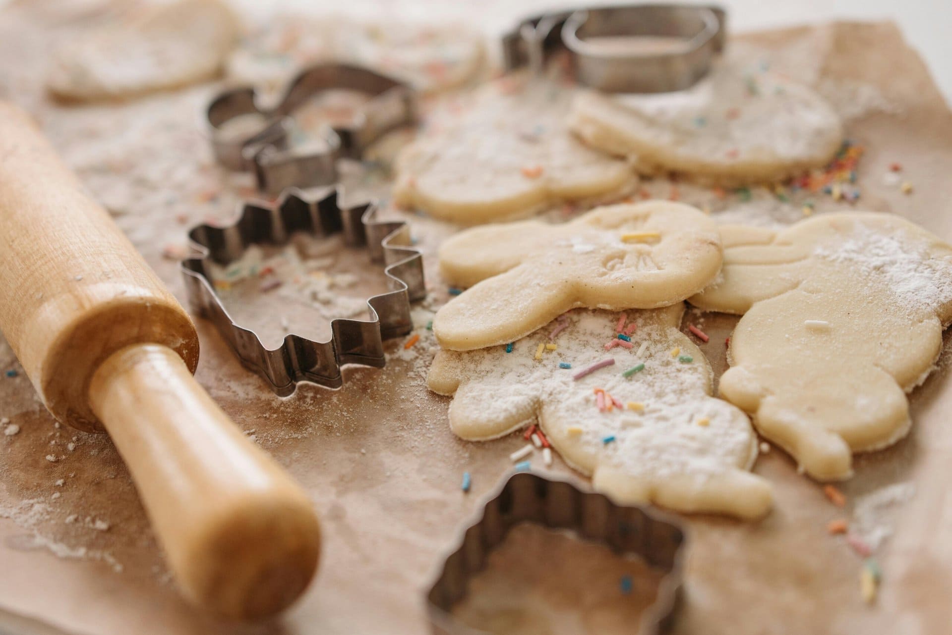 rolled cookie dough with animal shaped cookie cutters, a rolling pin, and colorful sprinkles on a parchment lined surface.
