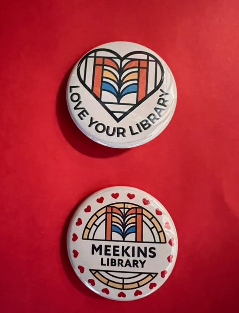 two round library themed buttons on a red background; one says "love your library" with a heart design, the other says "meekins library" with heart accents.