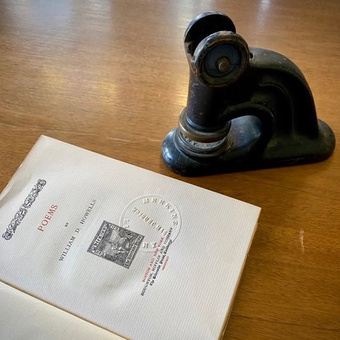a metal embosser rests on a wooden table next to an open book titled 