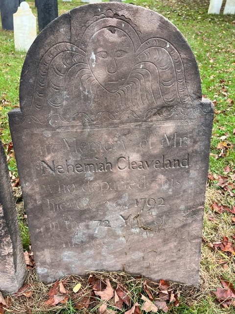 a weathered gravestone with an engraved angel face and wings, commemorating mrs. nehemiah cleaveland, who died in 1792 at age 72. the stone is set on grass with scattered leaves.
