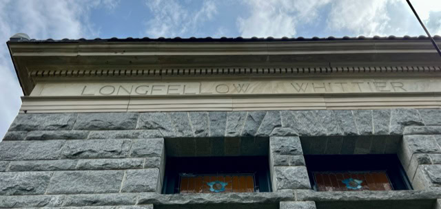 stone building facade with the names "longfellow" and "whittier" engraved above two upper windows; cloudy sky visible above the roofline.