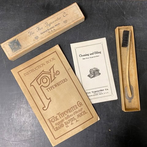 a fox typewriter co. instruction book, cleaning and oiling booklet, brush, and original packaging are displayed on a dark surface.