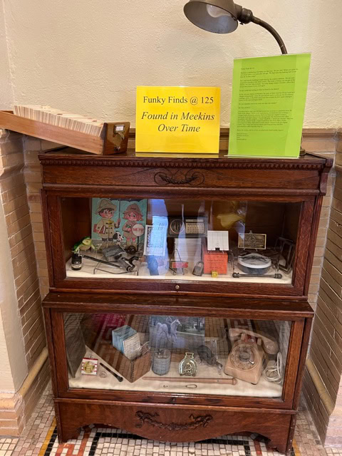wooden display cabinet with two shelves containing various small artifacts and memorabilia; sign on top reads "funky finds @ 125 found in meekins over time.