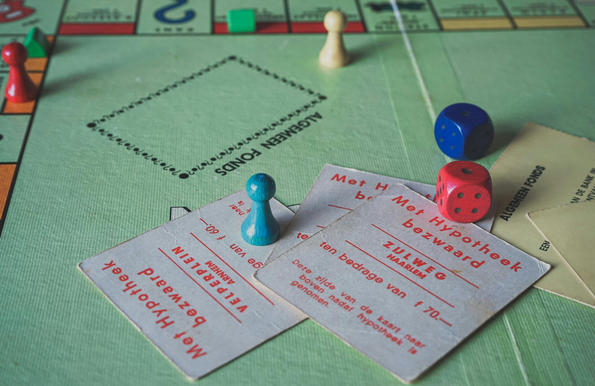 a close up of a monopoly board game in progress, showing game pieces, dice, and two dutch language cards on the board.
