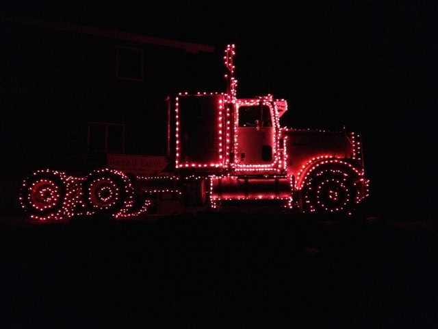 a semi truck decorated with red string lights is parked outside at night, with its outline illuminated against a dark background.