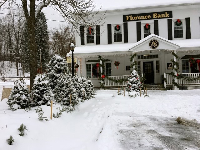 a white building labeled "florence bank" decorated with holiday wreaths, surrounded by snow covered trees and ground on a winter day.