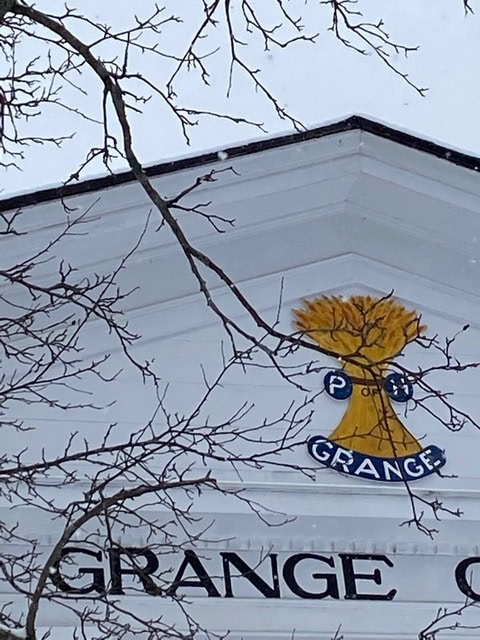 white building facade with the word "grange" and an emblem showing a yellow wheat sheaf above it; bare tree branches partially obscure the view.