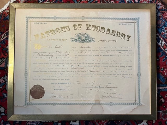 framed certificate from the patrons of husbandry, dated january 1874, with an official seal and signatures, displayed on a patterned rug background.