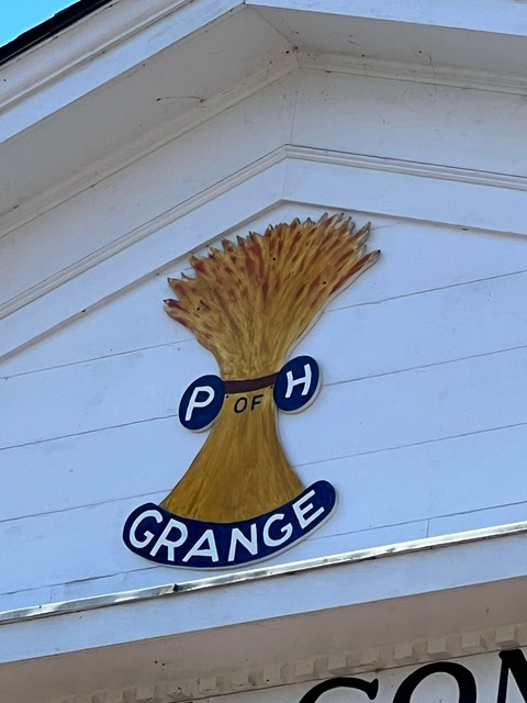a sheaf of wheat with the letters "p of h" and the word "grange" is displayed on the exterior wall of a white building.