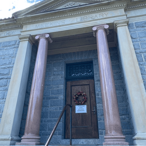 stone entrance of meekins library with two columns, wooden door, a wreath, and a sign that reads 