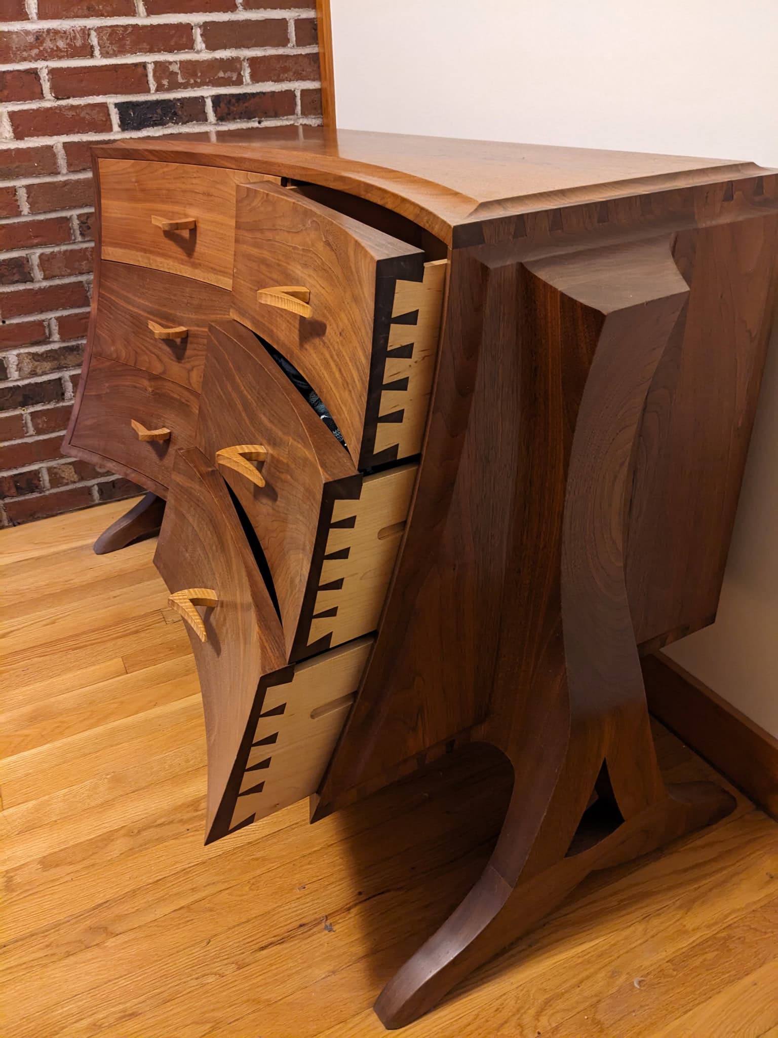 a wooden dresser with curved legs and body, featuring dovetail joints and three open drawers showing contrasting light and dark wood.