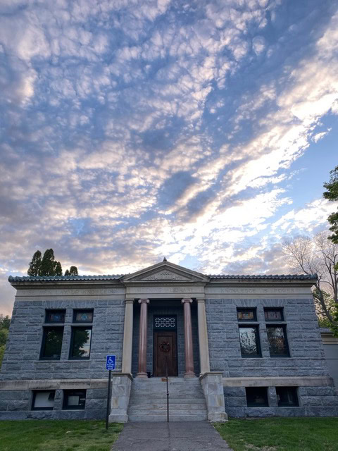 a small, gray stone building with columns at the entrance is pictured under a partly cloudy sky at dusk. a wheelchair accessible sign is visible near the front steps.